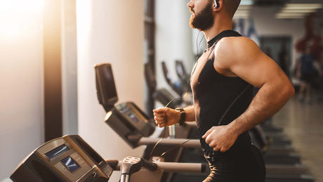 Man wearing blank tank top running on treadmill while looking out window.