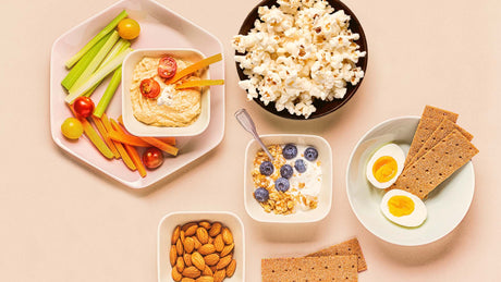 Assortment of snacks like veggies and hummus, popcorn, hard boiled eggs, and fruit bowlsl