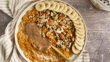 Bowl of Pumpkin Spice Protein Oatmeal with assorted nuts and banana on top.
