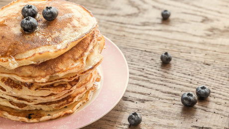 Kaizen Naturals Vanilla Protein Pancakes with blueberries on a pink plate on a table.